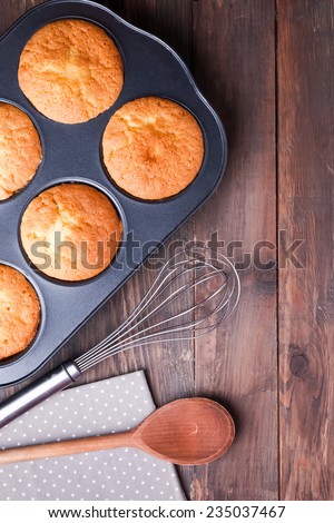 Baking tray with baked muffins, whisk and wooden spoon on the wooden table, top view