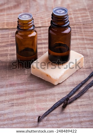 Bottles with aroma oil, vanilla pods and hand made soap on the wooden background. Spa still life.