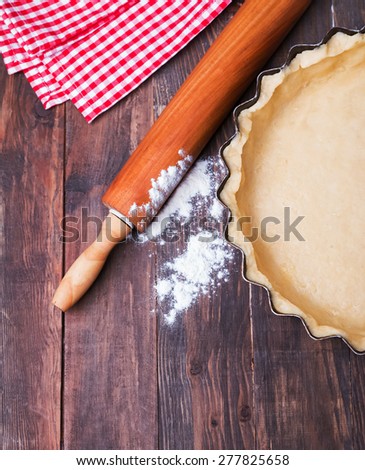 Making a tart. Baking pan with raw dough, rolling pin and flour on the wooden table