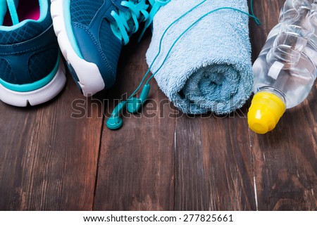 Sport equipment. Sneakers, water, towel and earphones on wooden background