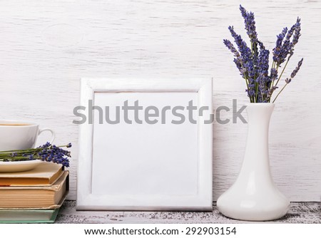 Frame with empty place for text or picture. White colored interior, vase with lavender flowers, books and cup of coffee. Mock up.