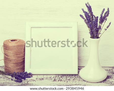 White colored frame with place for text or picture, lavender flowers in vase on white table. Retro toned photo.