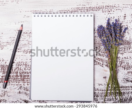 Empty notepad, pencil and lavender flowers on the white wooden background, top view.