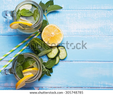 Lemon and cucumber detox water in glass jars on blue colored wooden background, top view