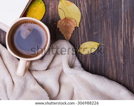 Cup of coffee, leaves and blanket on the wooden background, top view