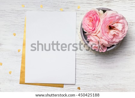 Blank paper and cute pink flowers on white wooden table, top view