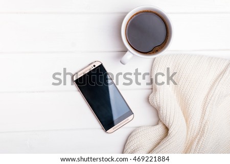 Coffee, phone and knitted sweater on the white table, top view