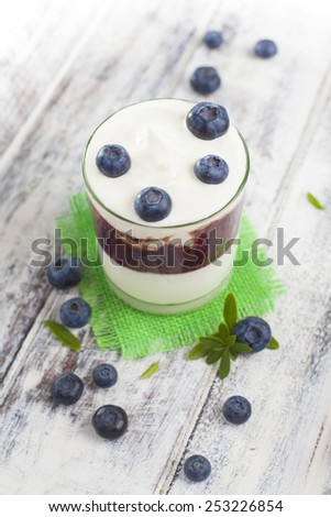Light breakfast setup with yogurt on white wooden table. Plane Greek style yogurt with jam and loose blueberries on heart shaped coaster over white painted grunge style wooden table.