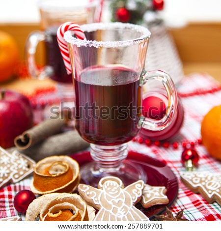 Two glasses of Mulled wine decorated with sugar rim and candy along with spices, fruit, gingerbread cookies and Christmas decorations on checkered red and green cloth.