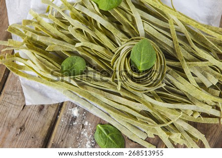 Raw homemade spinach pasta with spinach leaves over the rustic wooden table