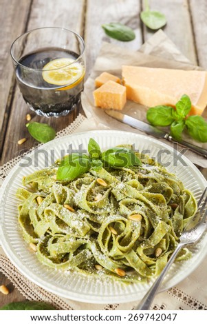 Cooked homemade spinach pasta with pesto, pine nuts, Parmesan cheese and basil leaves over the rustic wooden table