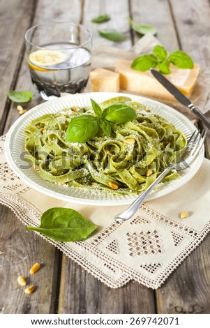 Cooked homemade spinach pasta with pesto, pine nuts, Parmesan cheese and basil leaves over the rustic wooden table