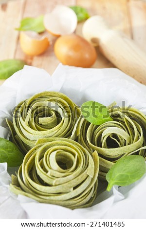 Raw homemade spinach pasta nests with spinach leaves and eggs over the rustic wooden table