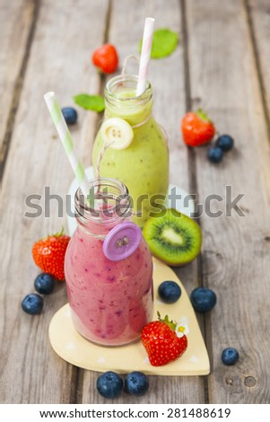 Fresh blended fruit smoothies in vintage milk bottles with berries on rustic wooden table