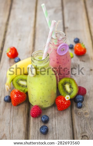 Fresh blended fruit smoothies in vintage milk bottles with berries on rustic wooden table