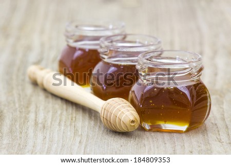 three jars of honey and honey dipper on wooden background