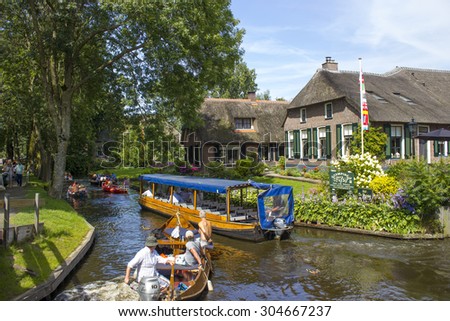 GIETHOORN, NETHERLANDS - AUGUST 05, 2015: Unknown visitors in the sightseeing boating trip in a canal in Giethoorn. The beautiful houses and gardening city is know as \