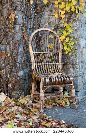 Old wicker chair near stony wall in yellow fallen leafs