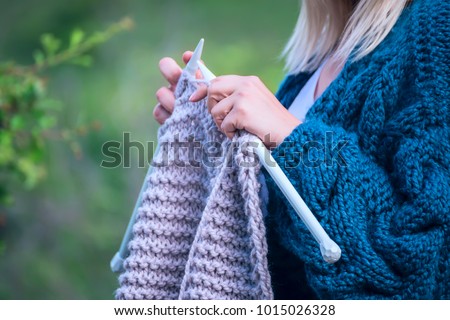 Knitting on knitting. Hands close-up knitting on knitting needles, gray wool knit against the backdrop of a natural garden. Needlework in the garden.