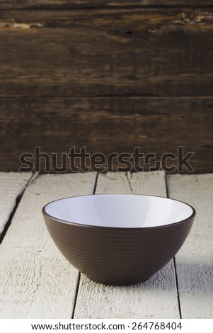 Salad bowl brown and white blank on white textured boards illuminated with soft light.