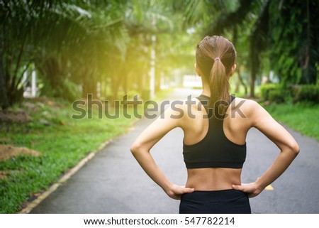 Back view of young fitness woman running on the road in the morning. People and sport concept, Sun light flare, Selective focus