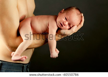 young father holding his newborn son carefully over black