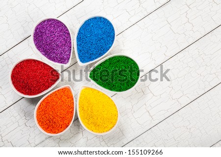 A rainbow assortment of colorful baking sprinkles used for decorating cookies and cakes in petal shaped bowls.