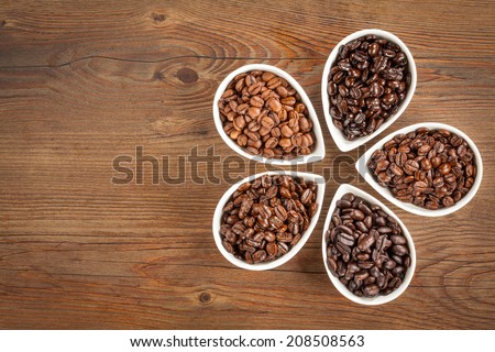Overhead view of several varieties of fresh roasted coffee beans on a brown wooden background with copy space.