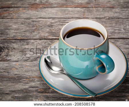 A blue coffee cup full of black coffee with a spoon on a rustic wood background.