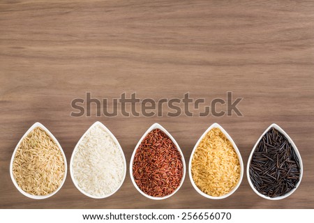 A colorful variety of rice in bowls, arranged as a border, over a wooden background