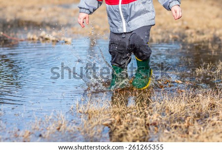 Little boy running in puddles wearing rain boots.