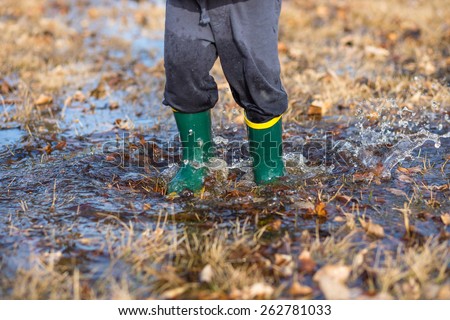 Toddler jumping in puddles wearing rubber boots. Shallow DOF. Focus is on boots and water.
