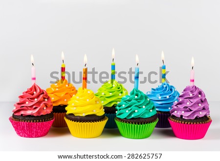 Rows of colourful cup cakes decorated with birthday candles and sprinkles.