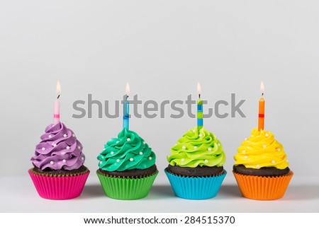 Four colorful cupcakes decorated with birthday candles and sprinkles.