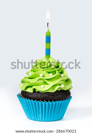 Chocolate Cupcake decorated with green icing, sprinkles and a lit birthday candle on a white background.