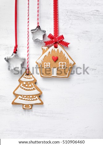 Gingerbread House and Christmas Tree cookies with red ribbon hanging over a white painted background.
