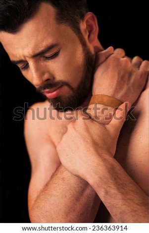 A bearded man holding his injured neck, isolated on a black background.