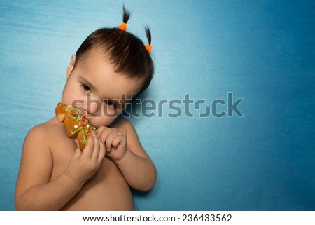 portrait of young infant adorable baby girl sitting on blue background and eating cookie