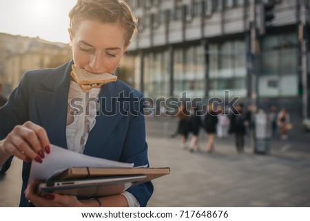 Busy woman is in a hurry, she does not have time, she is going to eat snack on the go. Worker eating and talking on the phone at the same time..  Business female person.