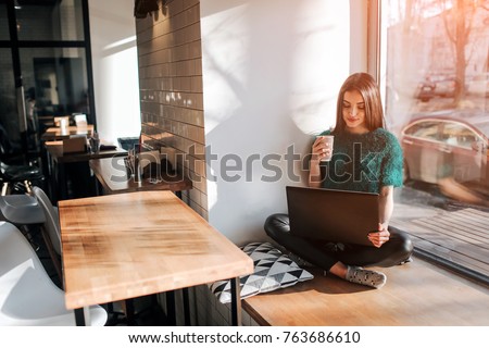 Beautiful brunette using laptop in cafe. Young attractive woman is making plans for the future, sitting in front of an open laptop computer in a cozy coffee shop.