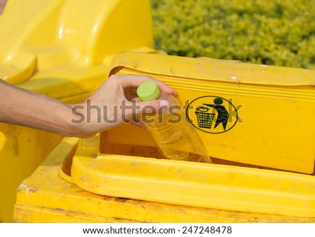 Hand throwing empty bottle in the yellow litter bin.