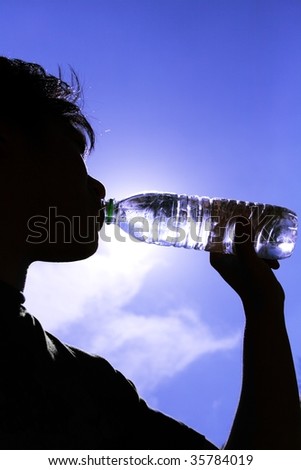 Silhouette of a man drinking from a plastic bottle shot against a blue sky