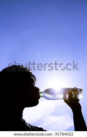 Silhouette of a man drinking from a plastic bottle shot against a blue sky  face