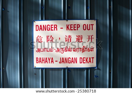Danger keep out warning sign against blue metal in four languages: English, Chinese, Tamil and Malay