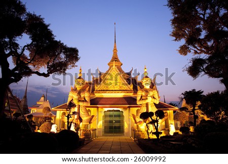 Thai temple with a golden glow and guarded by two huge statues. Shot with a view of blue evening sky in Bangkok, Thailand