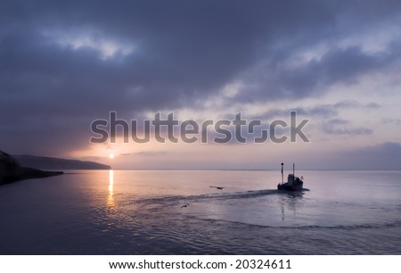 Fishing boat heading out to sea at dawn, Beer, Devon, UK
