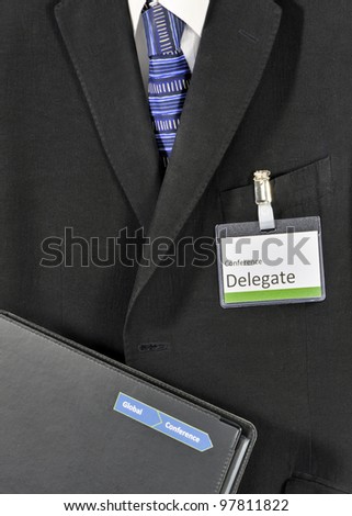 Closeup on male business suit with conference folder and delegate badge. The conference logo has been falsified
