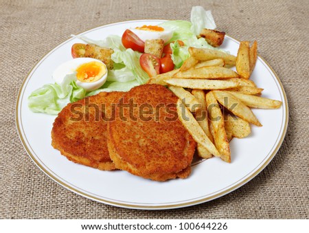 A meal of chicken burgers with french fried potato chips and a tomato, egg and lettuce salad