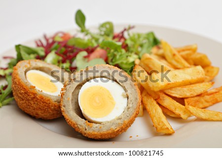 A Scotch egg - a hard boiled egg wrapped in breaded sausage meat and deep fried - served with chips (french fries) and a salad of lettuce, tomato and grated beetroot