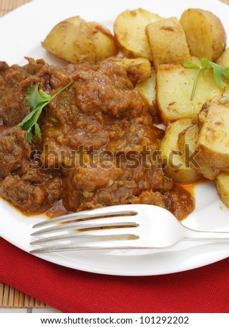 A madras butter beef curry served with curried potatoes and garnished with coriander leaves